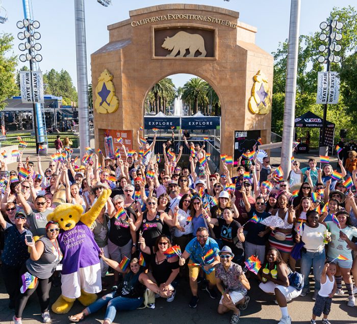 A large crowd of people posing together for a group photo with CA State Fair mascot, Poppy, at the Fair. For Out at the Fair group photo 2019