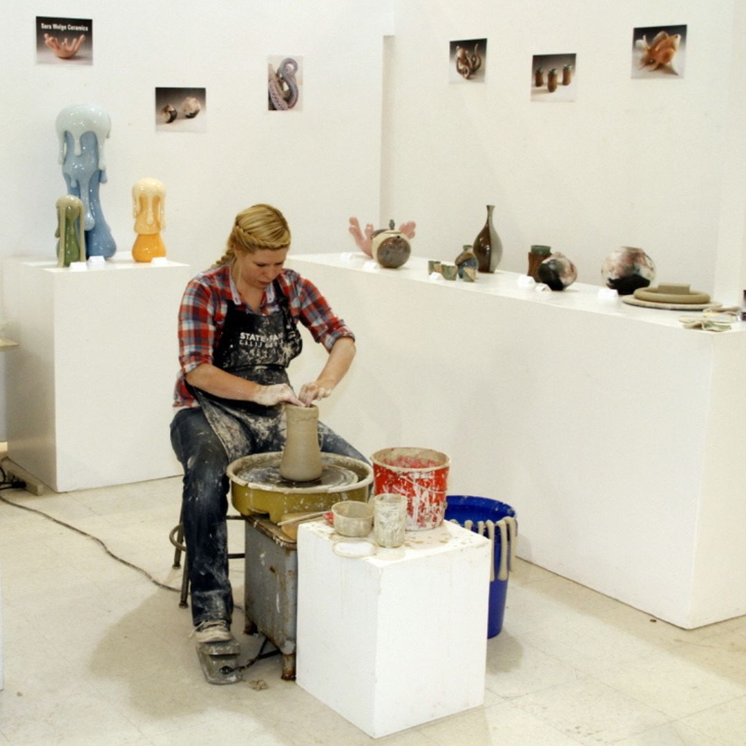 Woman demonstrating how to make a clay pot. Behind her are clay pots on display