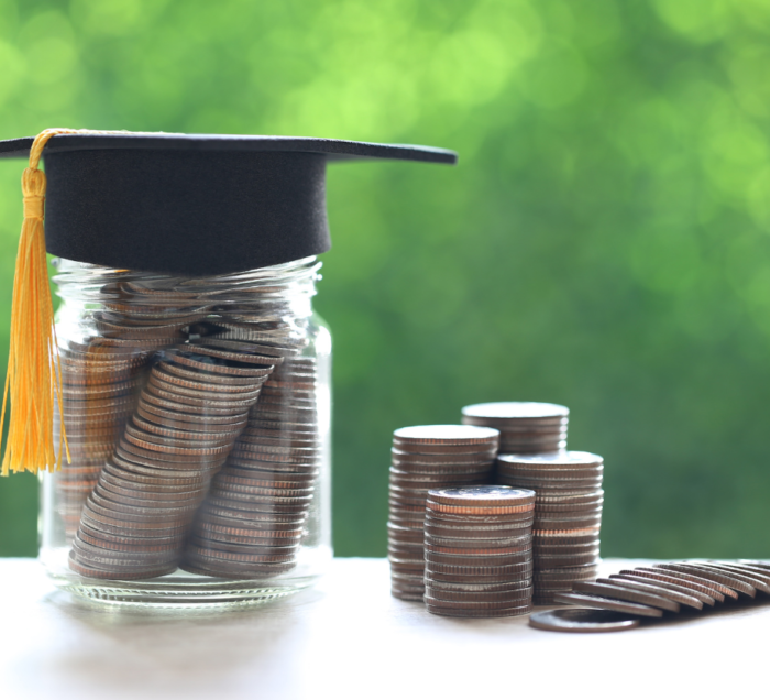 A jar of coins with a graduation cap on top. To the right is a stack of coins.